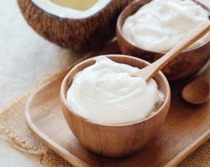 Close-up of thick, creamy coconut yogurt served in small wooden bowls with wooden spoons, accompanied by fresh coconut halves in the background on a rustic wooden tray