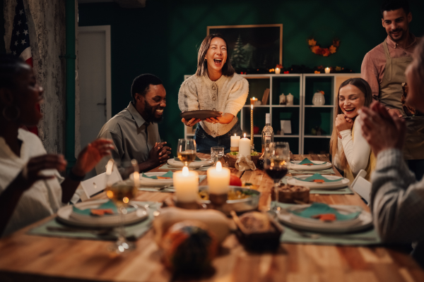 A joyful group of friends gathered around a candlelit dinner table, laughing and sharing a cozy low-sugar winter meal together in a warm, festive home setting.