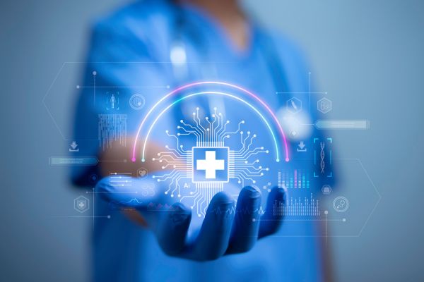 A healthcare worker in blue scrubs holds out a hand with a glowing digital medical cross and circuit-style graphics, symbolizing AI and technology in modern healthcare.