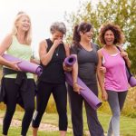 Group of midlife women walking outdoors with yoga mats, representing movement and hormone balance in midlife.
