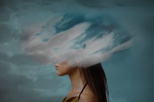 Surreal portrait of a woman in profile with clouds obscuring her head, symbolizing brain fog, mental fatigue, or emotional overwhelm