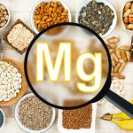 Assortment of magnesium-rich foods, including almonds, pumpkin seeds, peanuts, beans, sunflower seeds, and bananas, surrounding a magnifying glass highlighting the chemical symbol “Mg” for magnesium.