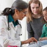 Pediatrician examining a child with her mother during an evaluation for symptoms that may be related to Vitamin C deficiency and modern scurvy.