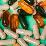 Assorted beige capsules and amber and dark green softgel supplements scattered across a bright turquoise surface.