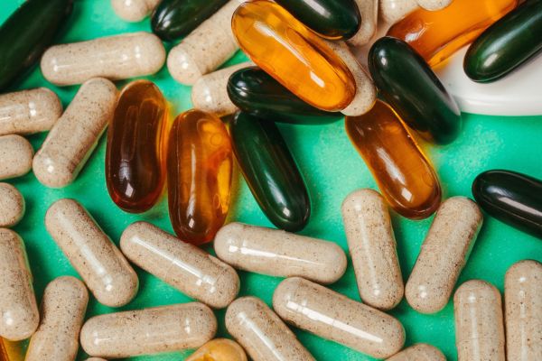 Assorted beige capsules and amber and dark green softgel supplements scattered across a bright turquoise surface.